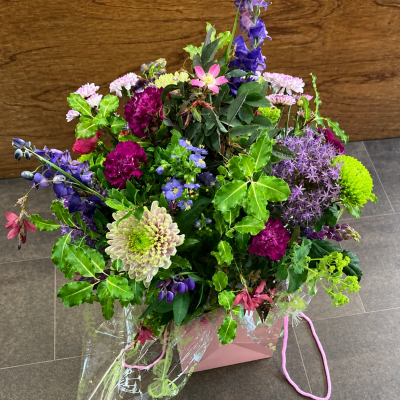 Wild Garden Symphony - A vibrant, free-flowing arrangement inspired by the beauty of an untamed garden in full bloom. Rich jewel tones blend with soft pastel accents and fresh greenery, creating a lively and expressive display. The mix of textures and natural movement gives this piece a relaxed, just-gathered feel, while still maintaining a sense of balance and artistry. Perfect for making a bold impression or celebrating life’s colourful moments, this design is full of character, charm, and natural elegance.