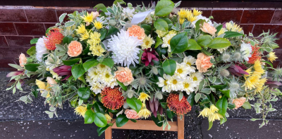 Autumn Meadow Casket Spray - A natural and uplifting casket spray inspired by the warmth and beauty of an autumn garden. Featuring soft peach, cream, and golden tones blended with textured foliage and seasonal details, this arrangement creates a heartfelt tribute filled with warmth, comfort, and treasured memories.
